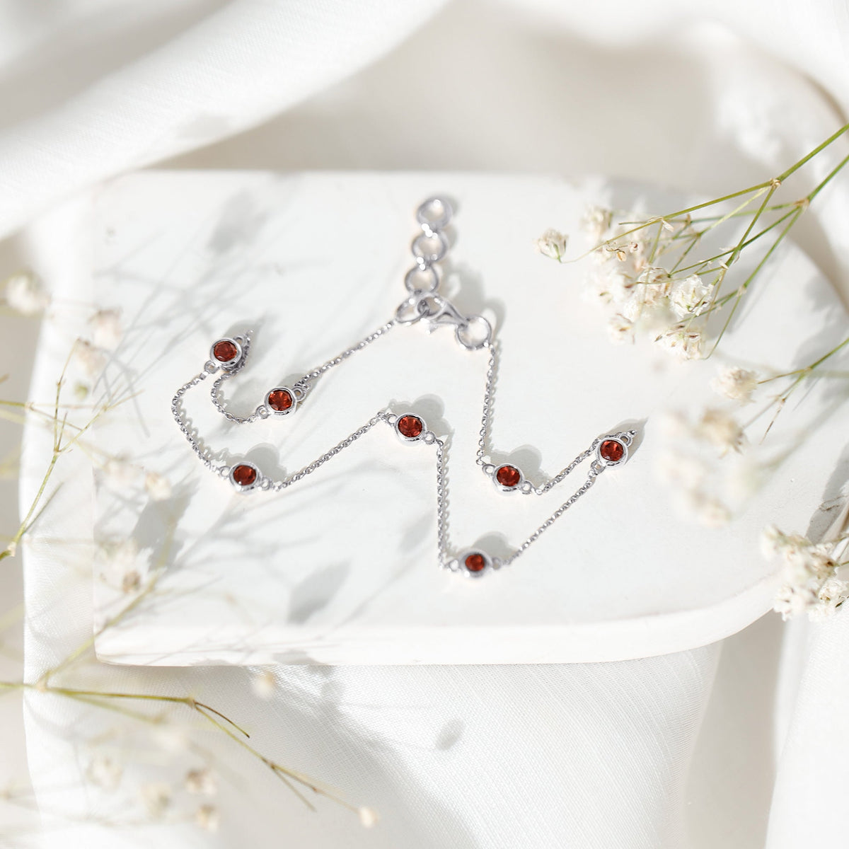 Bezel set garnet seven-stone station chain bracelet by Rosec Jewels showcasing sparkling red gemstones on a delicate gold chain.
