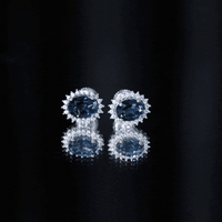 Rosec Jewels 6x8mm oval London Blue Topaz stud earrings with moissanite halo, showcasing sparkling blue gemstones and radiant design.