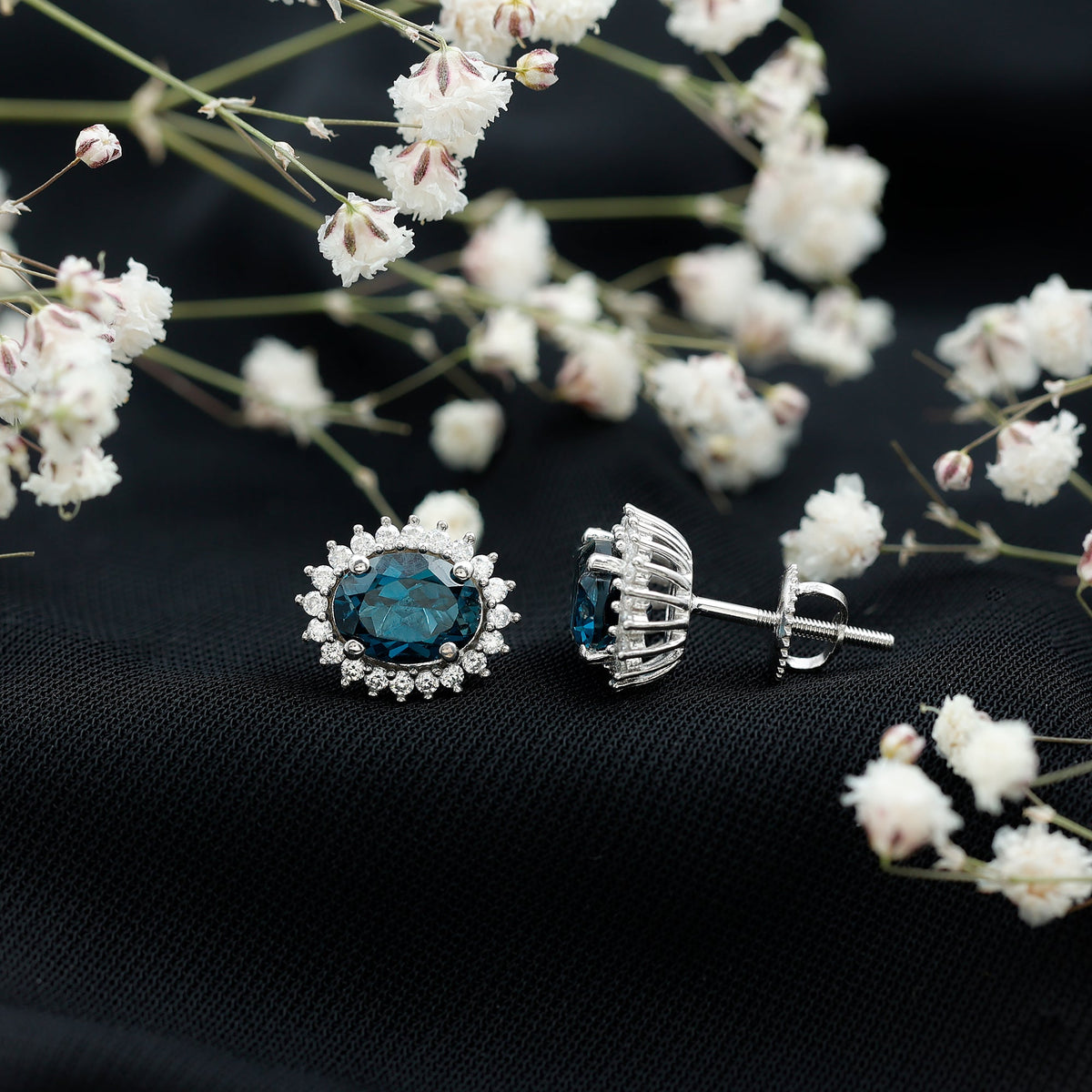 Rosec Jewels 6x8mm oval London Blue Topaz stud earrings with a Moissanite halo setting, featuring sparkling gemstone accents.