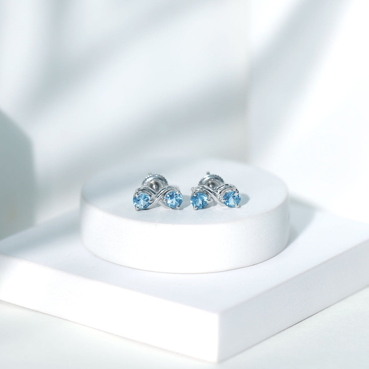Rosec Jewels real aquamarine infinity stud earrings with sparkling blue gemstones on silver posts.