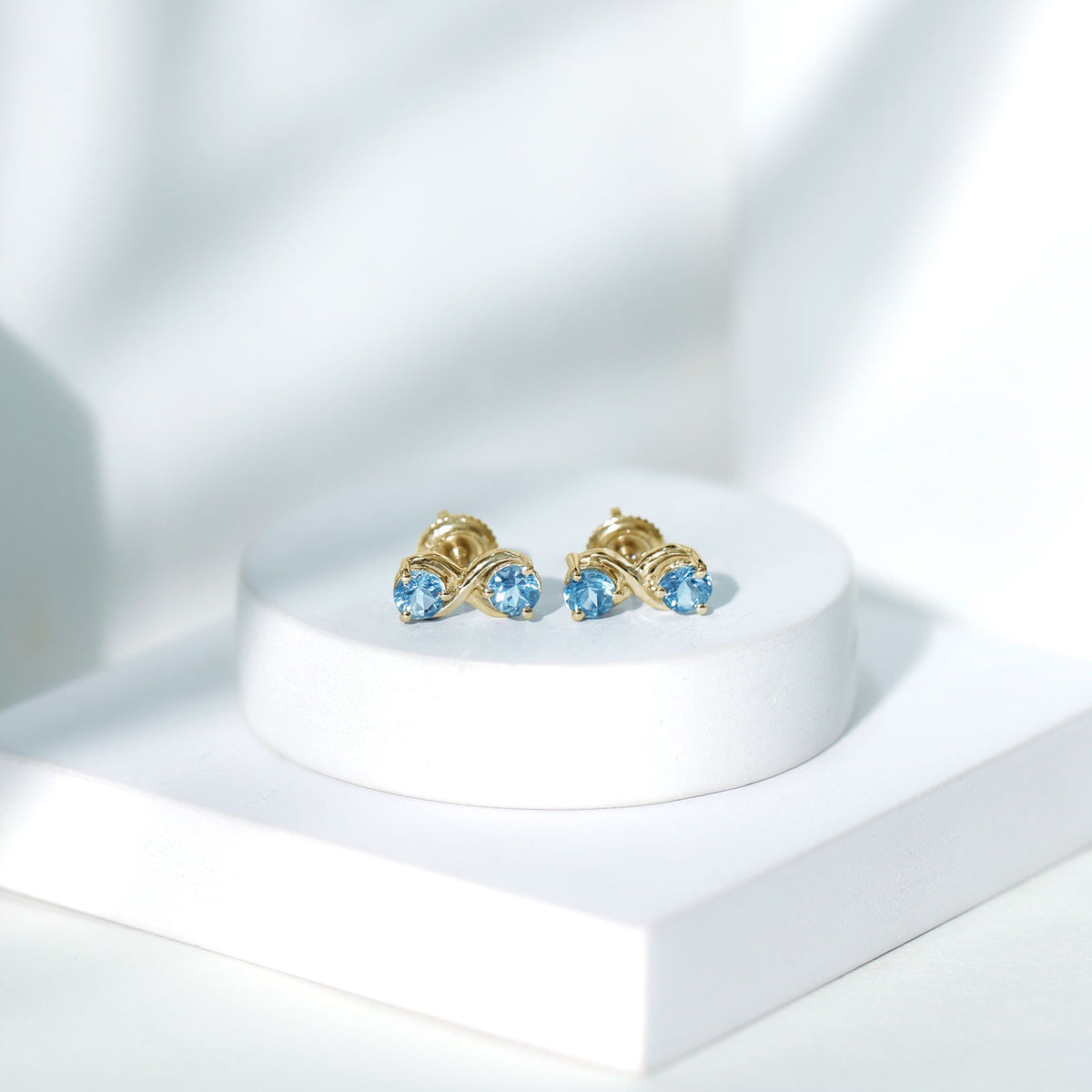 Rosec Jewels real aquamarine infinity stud earrings featuring sparkling blue aquamarine stones on silver posts.