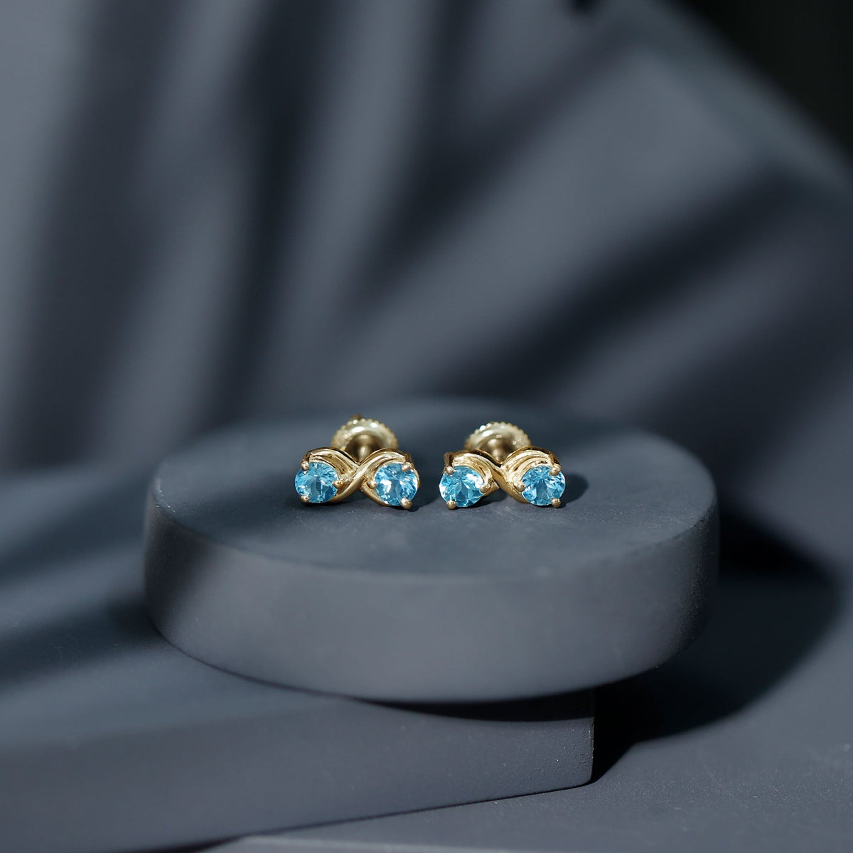 Rosec Jewels real aquamarine infinity stud earrings featuring sparkling blue aquamarine stones on silver settings.