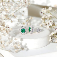 Rosec Jewels classic emerald stud earrings with diamond halo, featuring sparkling green gemstones and elegant metal setting.