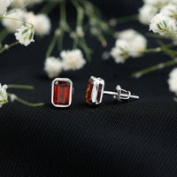Emerald cut 1.4 CT garnet solitaire stud earrings in bezel setting by Rosec Jewels, showcasing the deep red gemstone and sleek design.
