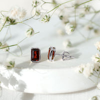 Emerald cut garnet solitaire stud earrings in bezel setting by Rosec Jewels, showcasing deep red gemstone on a sleek metal post