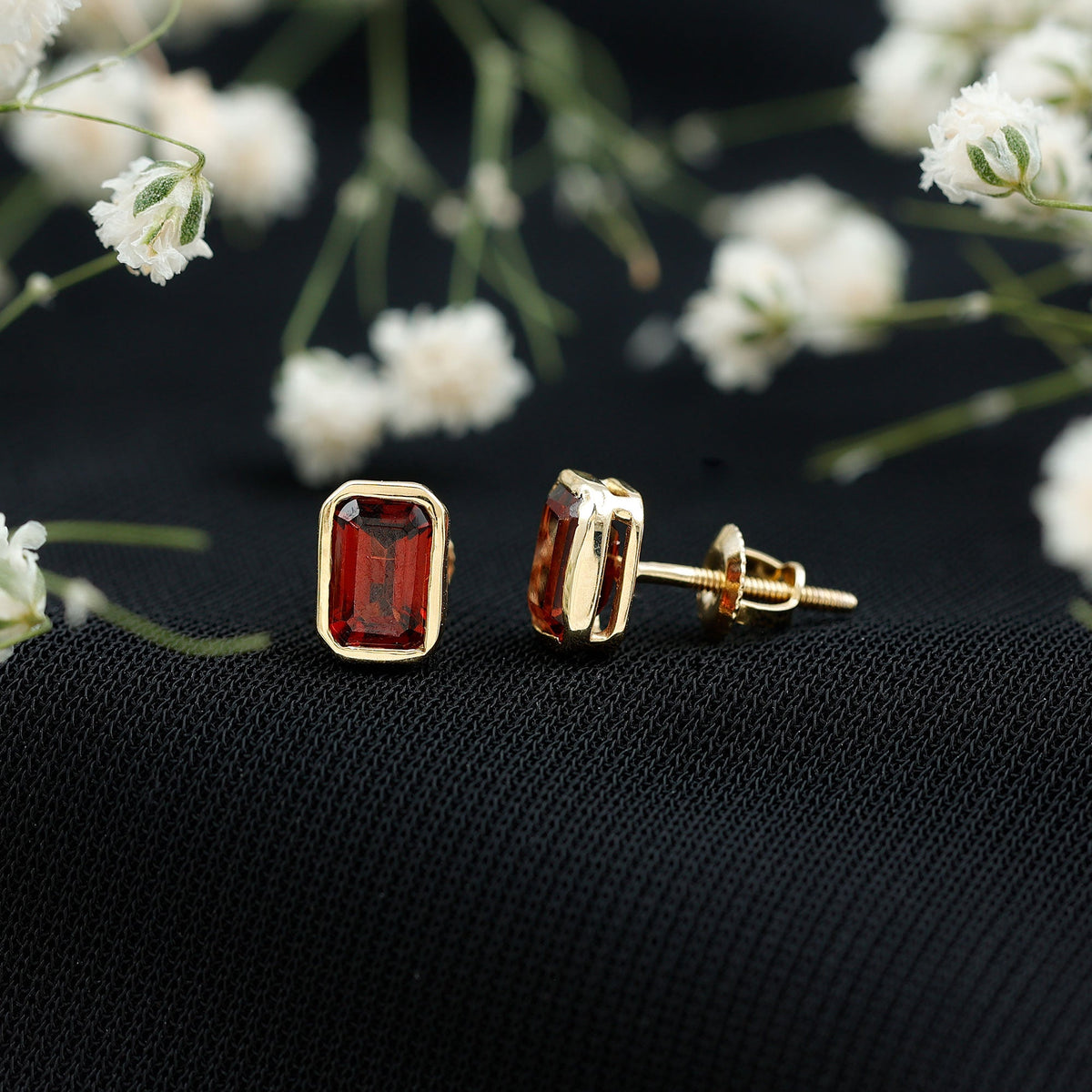 Emerald cut garnet solitaire stud earrings in bezel setting by Rosec Jewels, showcasing vibrant red gemstone on silver posts.