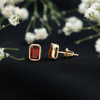 Emerald cut garnet solitaire stud earrings in bezel setting by Rosec Jewels, showcasing vibrant red gemstone on silver posts.