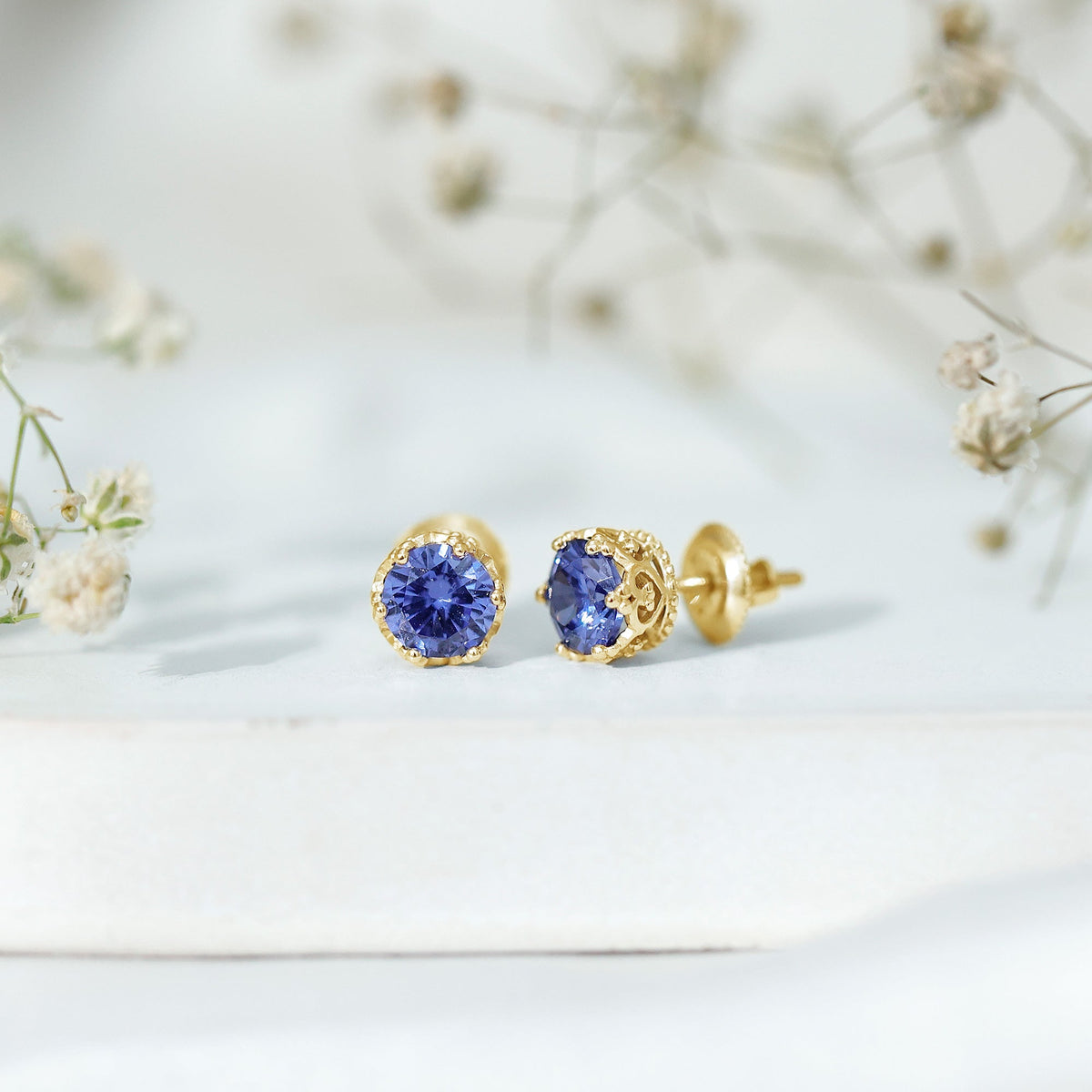 Created blue sapphire solitaire crown stud earrings by Rosec Jewels, featuring sparkling blue sapphires in elegant gold settings.