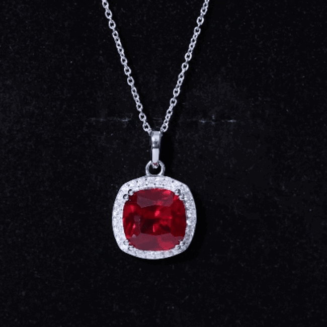 Cushion cut lab-grown ruby pendant with halo of moissanite stones on a silver chain, showcasing elegant jewelry design.