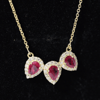 Pear cut lab-created ruby three-stone pendant with moissanite halo from Rosec Jewels, featuring a yellow background.