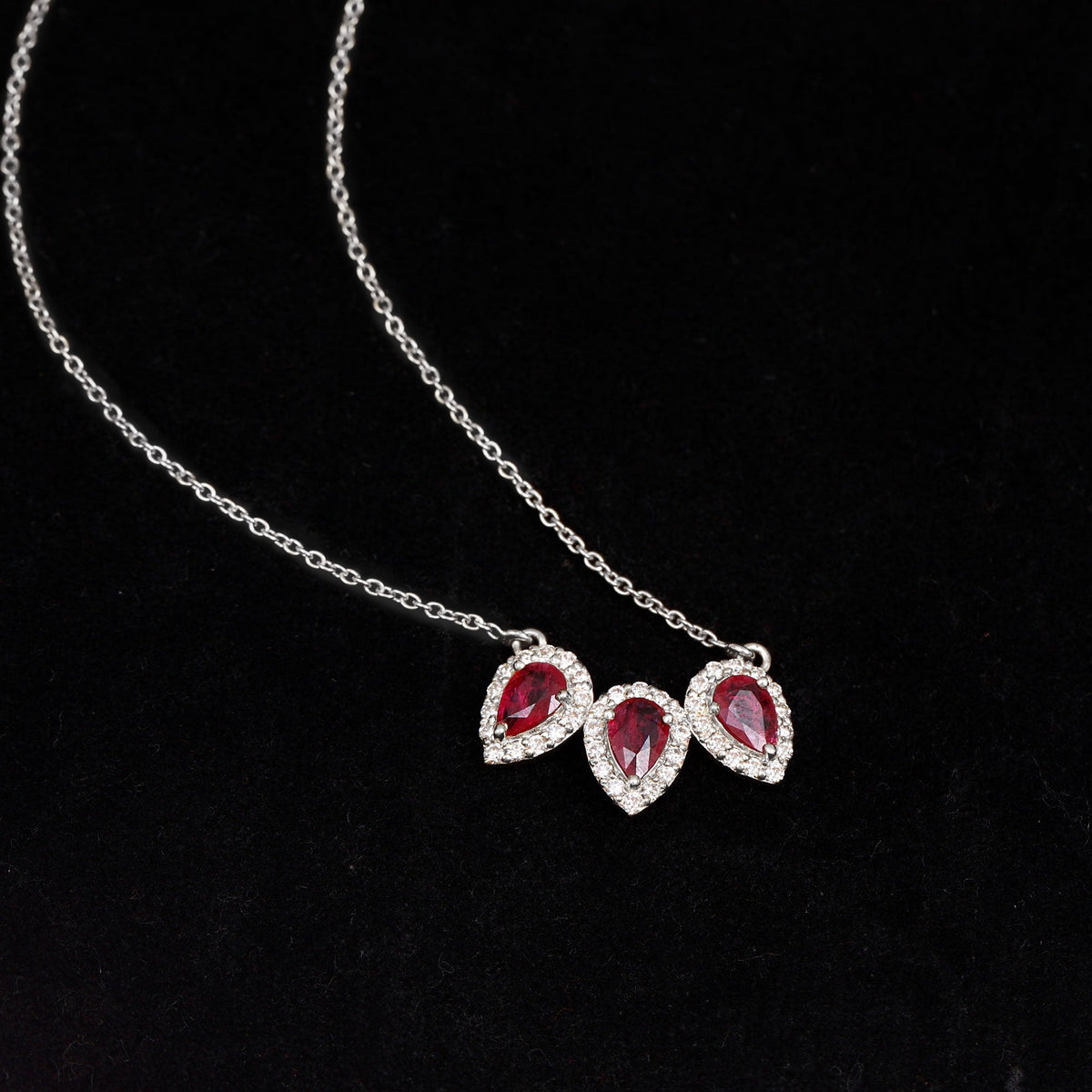 Pear-shaped lab-created ruby three-stone pendant with moissanite halo from Rosec Jewels, featuring a silver chain and elegant design.