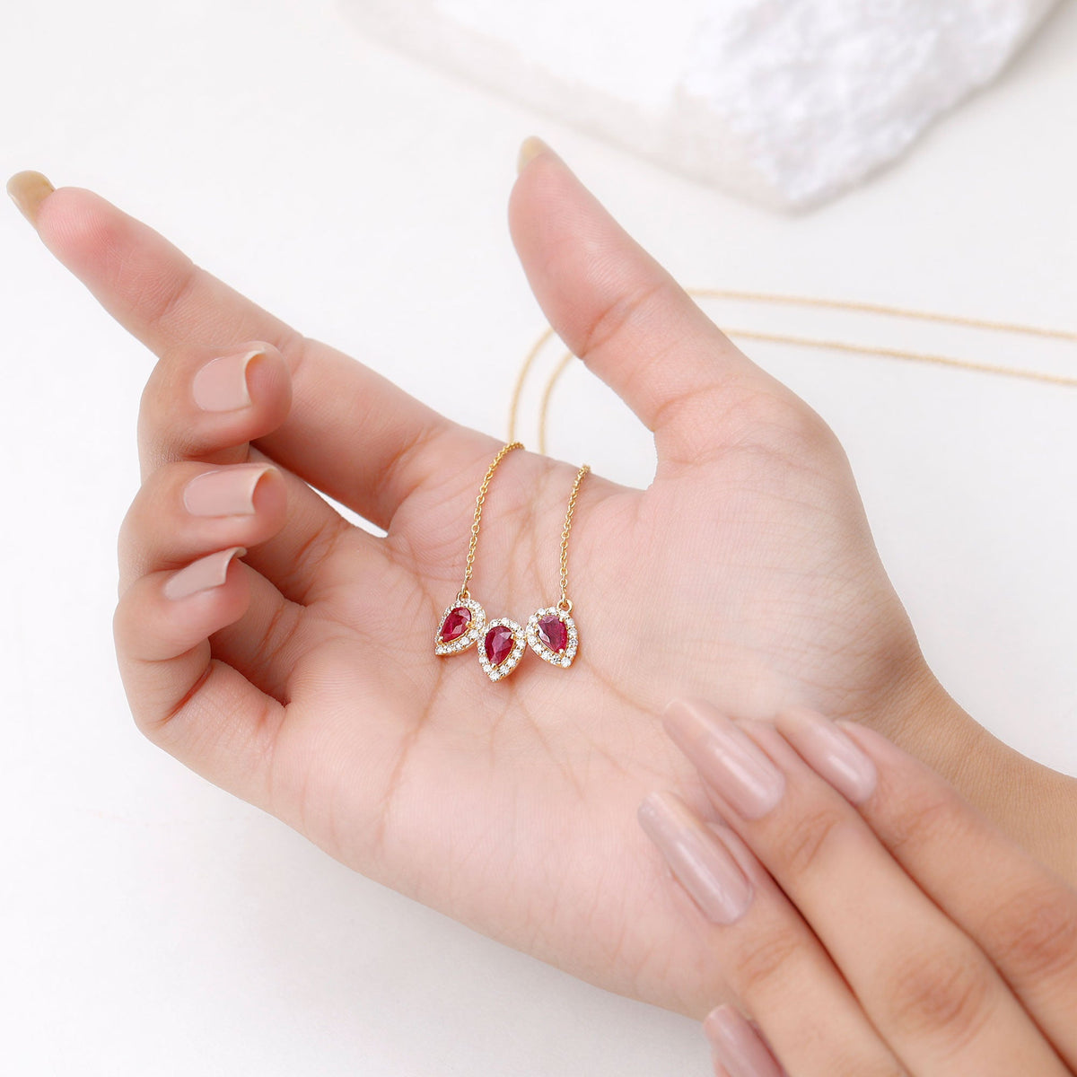 Pear cut lab-created ruby three-stone necklace with moissanite halo pendant by Rosec Jewels, showcasing vibrant red gemstones and sparkling accents.