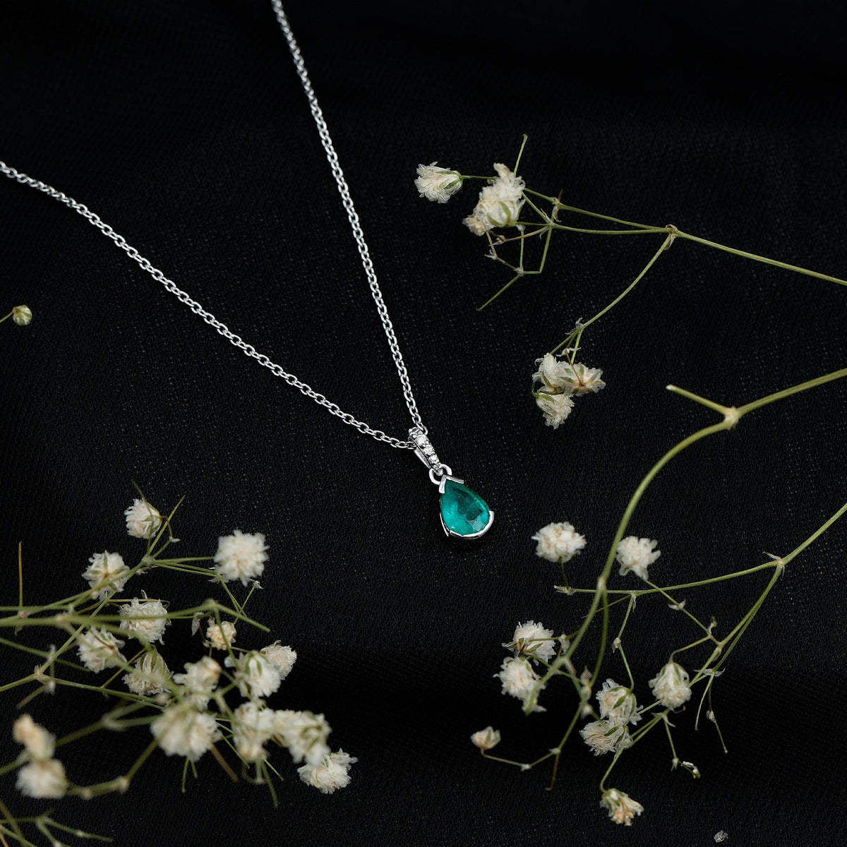 Pear cut emerald solitaire pendant with diamond accent bail, featuring a Rosec Jewels pendant design on a chain.