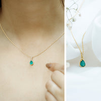 Pear cut emerald solitaire pendant with diamond accent bail, featuring a sleek rose gold setting and elegant jewelry design.