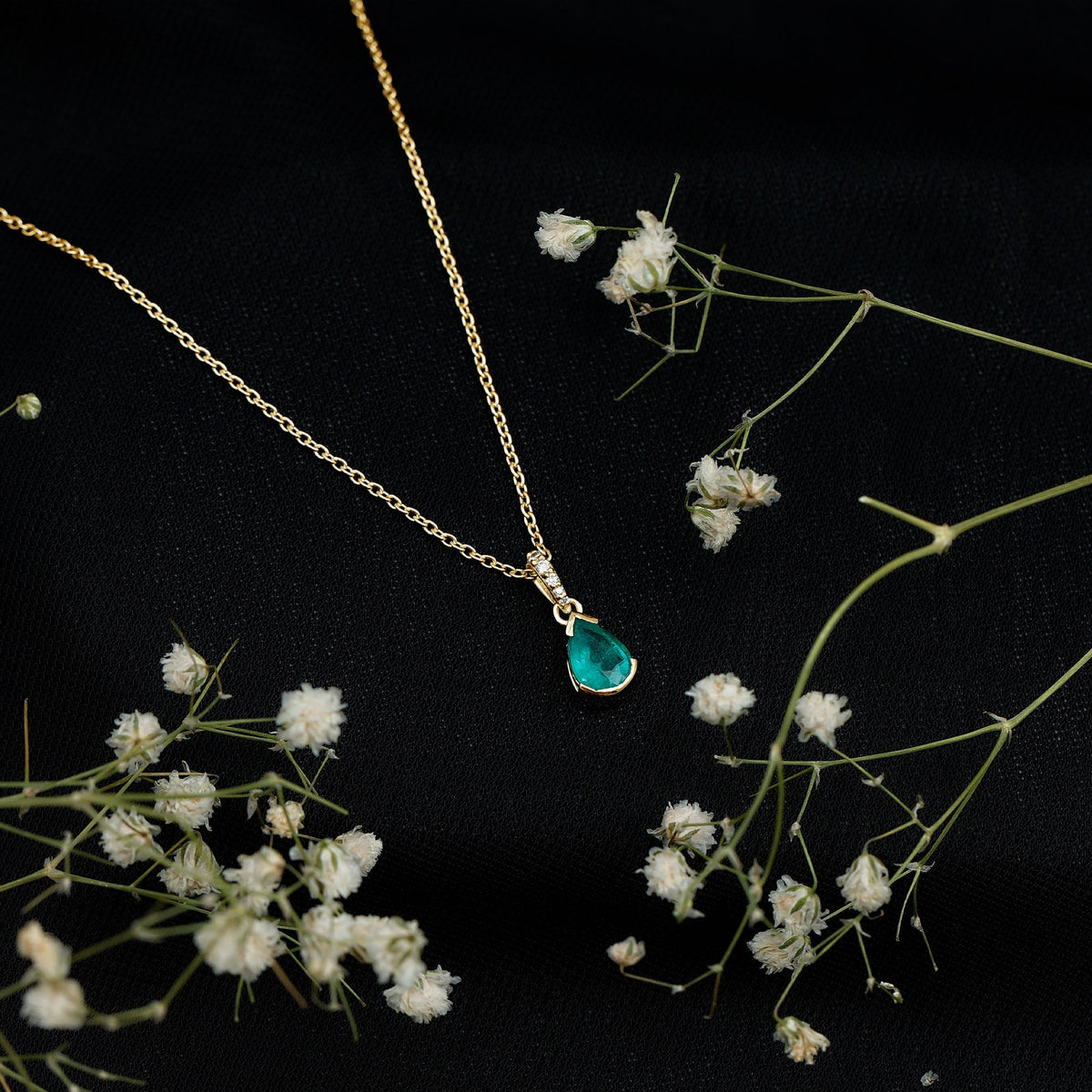 Pear cut emerald solitaire pendant with diamond accent bail by Rosec Jewels, showcasing a elegant green gemstone and sparkling accents.