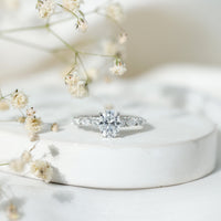 Oval moissanite solitaire engagement ring in claw setting with a silver band, showcasing a sparkling central gemstone.