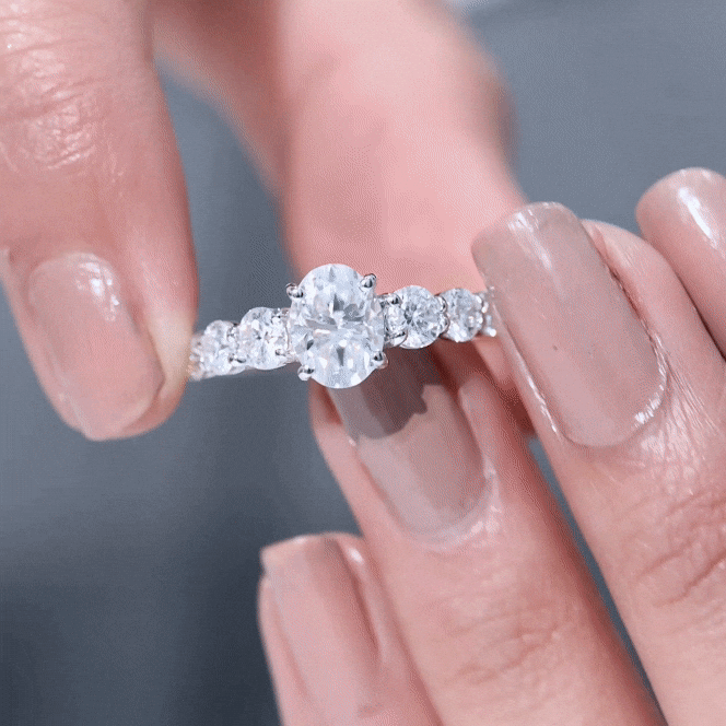 Oval cut moissanite side stone engagement ring with a 1.2 carat center, featuring sparkling white stones and a detailed band.
