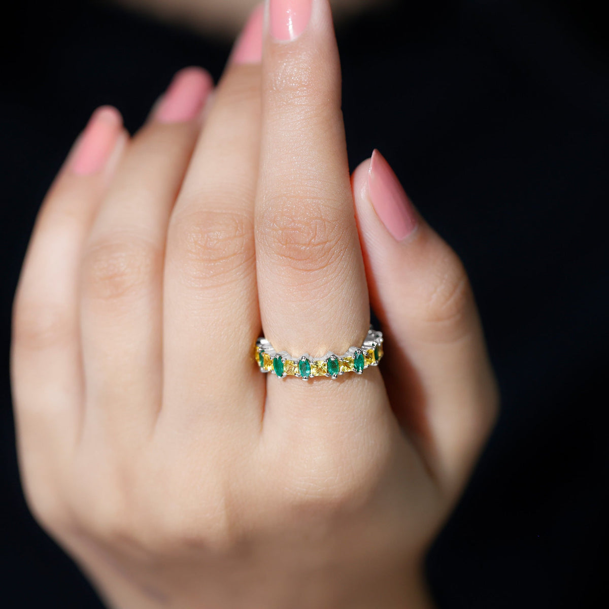 Designer yellow sapphire and emerald eternity wedding ring featuring alternating gemstones and intricate band details.