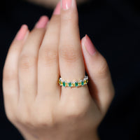 Designer yellow sapphire and emerald eternity wedding ring featuring alternating gemstones and intricate band details.