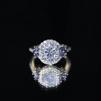 Yellow gold halo engagement ring with a 3-carat lab-grown diamond and blue sapphire accent, featuring intricate detailing.