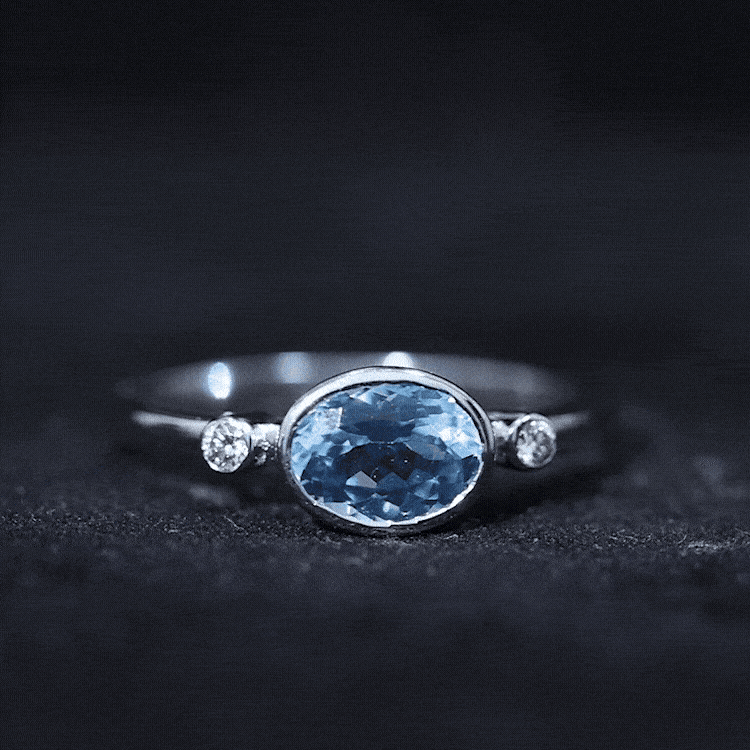 Bezel set aquamarine and diamond east-west engagement ring by Rosec Jewels featuring a central aquamarine gemstone and surrounding diamonds.