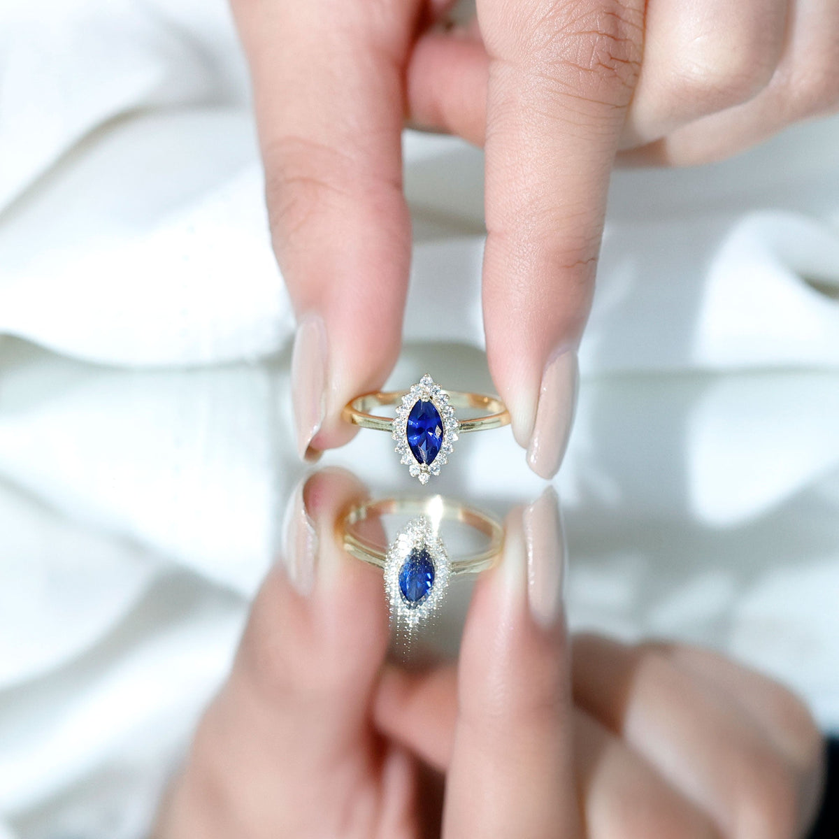 Marquise cut lab-grown blue sapphire engagement ring with diamond halo, featuring Rosec Jewels branding, displayed on a jewelry stand.