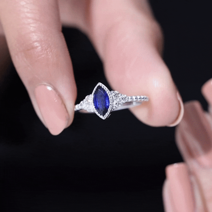 Vintage style 0.7 carat lab-grown blue sapphire marquise engagement ring with diamond trio by Rosec Jewels, displayed on a yellow background.