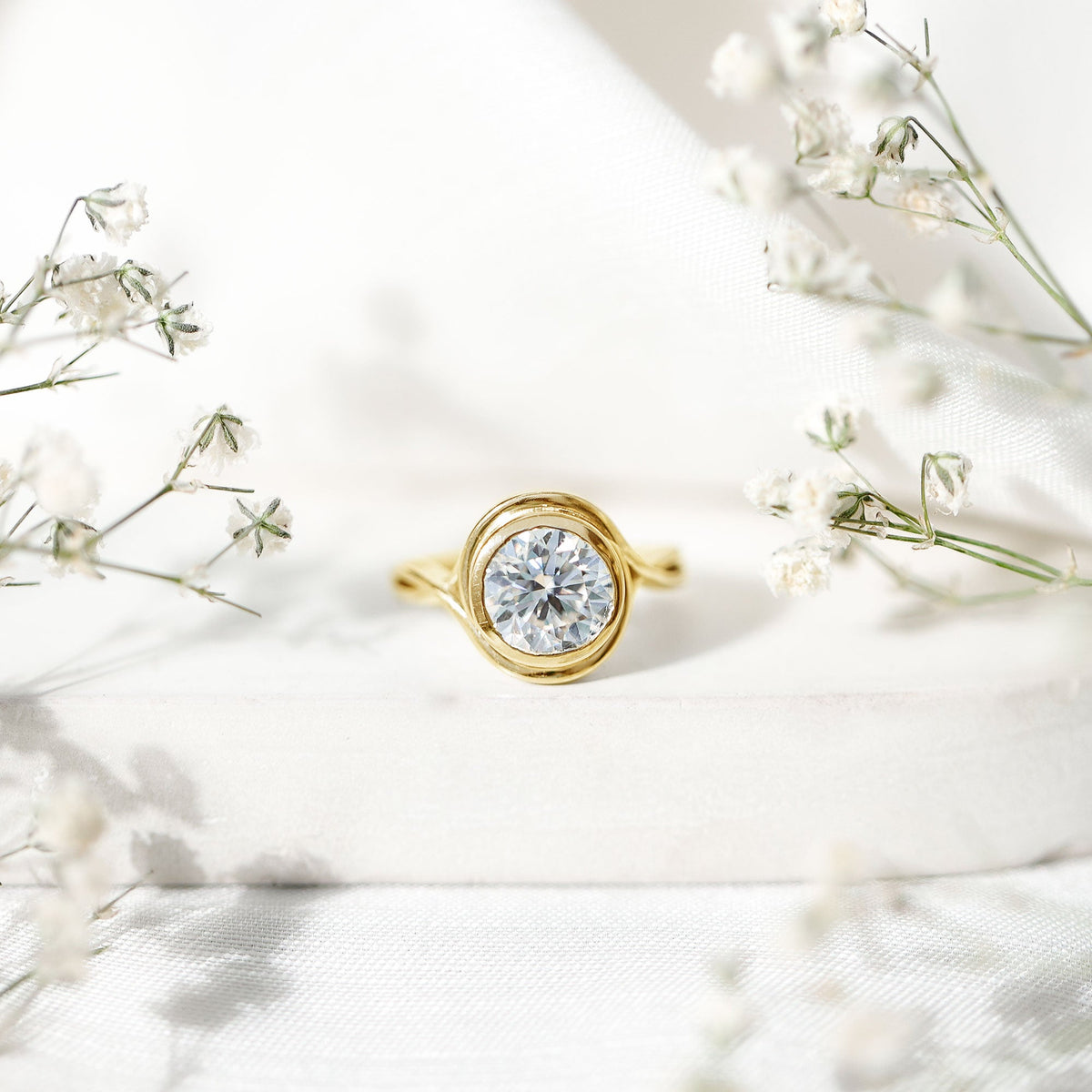 Rosec Jewels certified moissanite bezel set engagement ring with crossover shank, featuring a sparkling central stone and intricate band detail.