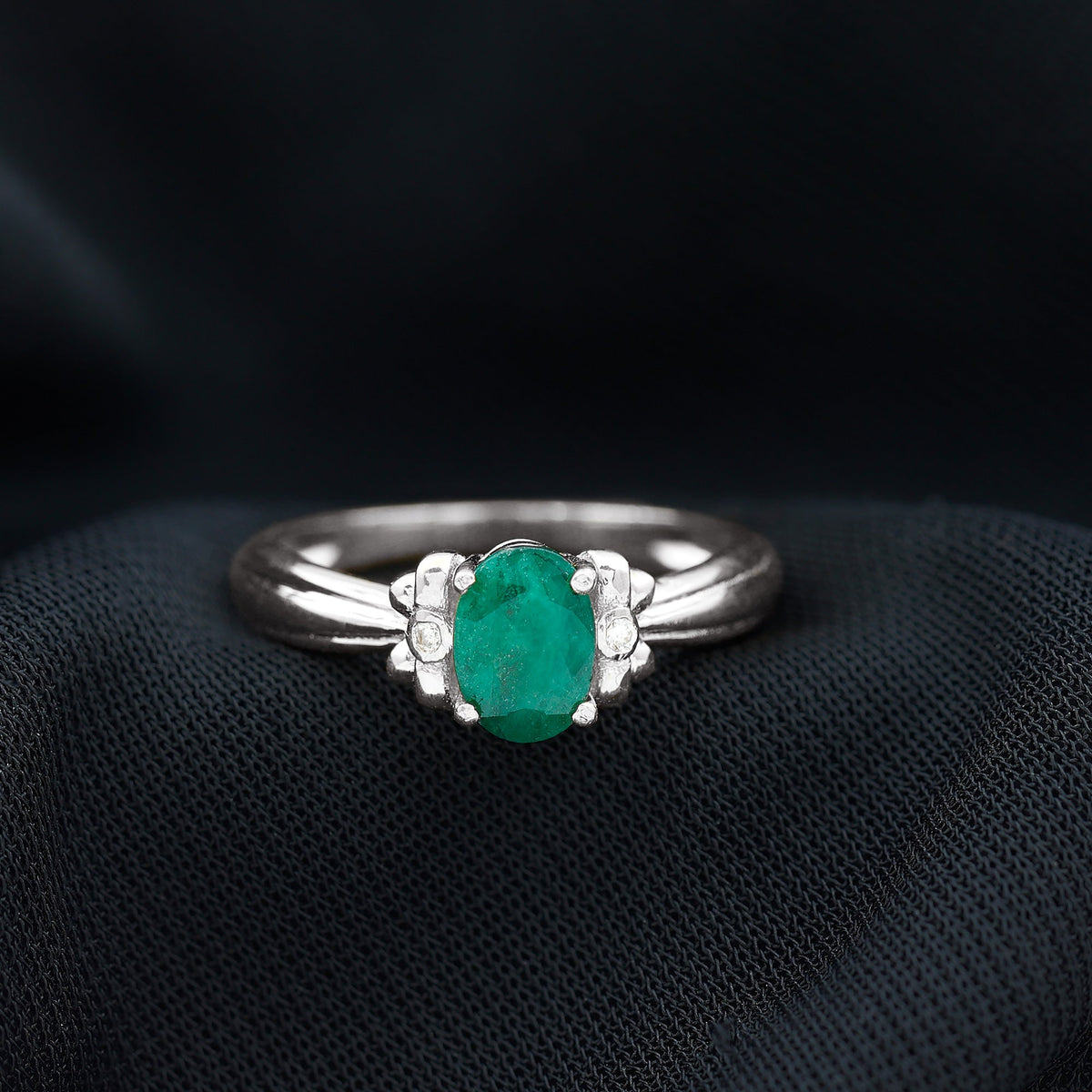 Oval cut emerald solitaire engagement ring with bow design from Rosec Jewels, featuring a detailed silver band and elegant setting.