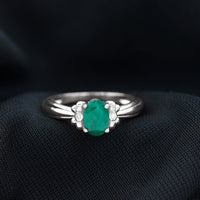 Oval cut emerald solitaire engagement ring with bow design from Rosec Jewels, featuring a detailed silver band and elegant setting.
