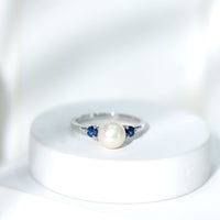 Cultured freshwater pearl engagement ring with blue sapphire accents, featuring a polished silver band and elegant design.
