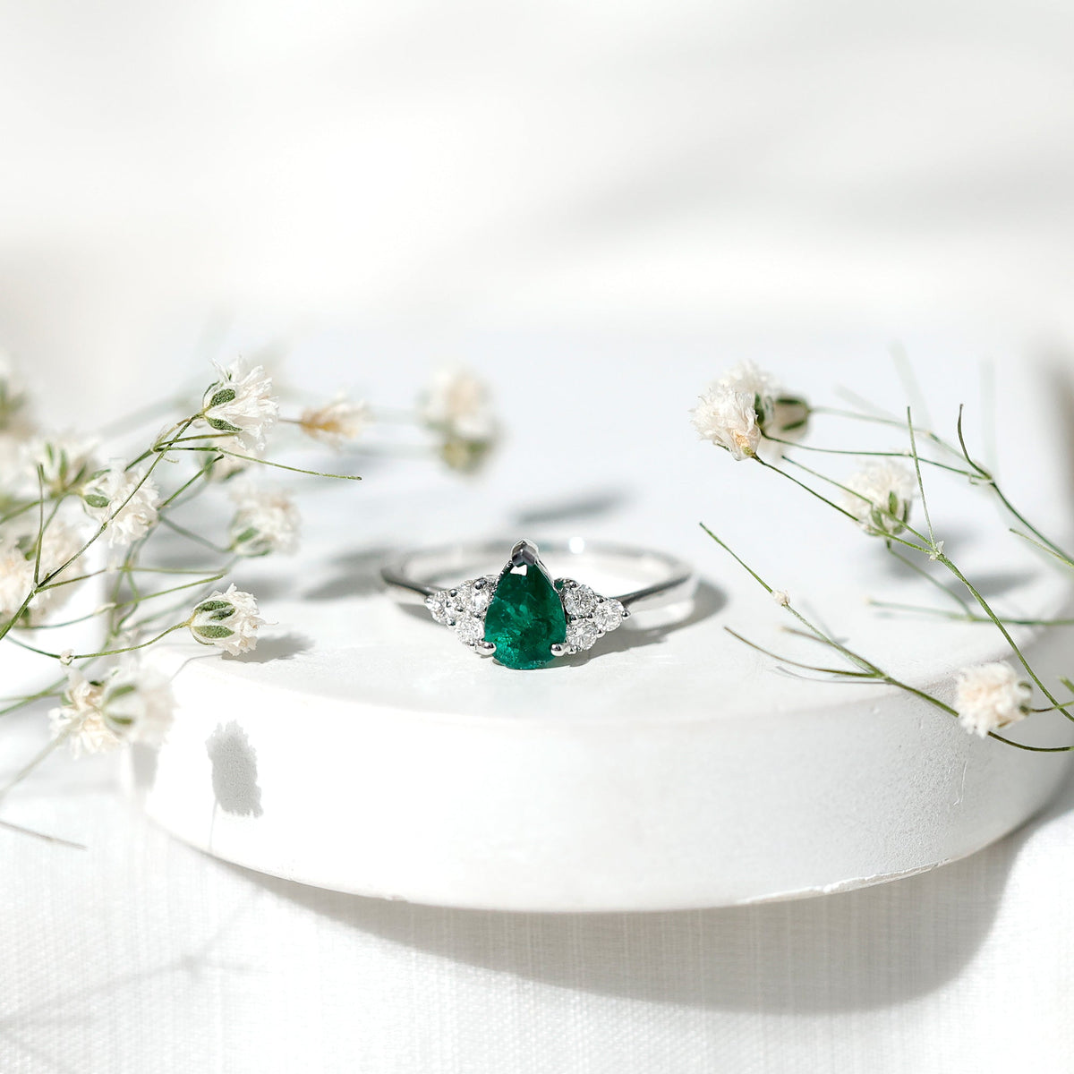 Pear-shaped emerald engagement ring with 0.6 carat AAA quality stone and diamond accents by Rosec Jewels, displayed on a ring holder.