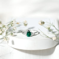 Pear-shaped emerald engagement ring with 0.6 carat AAA quality stone and diamond accents by Rosec Jewels, displayed on a ring holder.