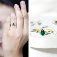 Pear-shaped emerald engagement ring with 0.6 carat AAA quality stone and diamond accents, featuring a delicate gold band.