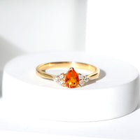 Pear-shaped fire opal engagement ring with diamond trio set in a Rosec Jewels ring, showcasing vibrant orange and white gemstones.