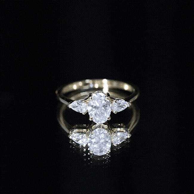 Yellow gold Oval and Pear Cut Moissanite three-stone engagement ring featuring elegant side stones and a polished band.