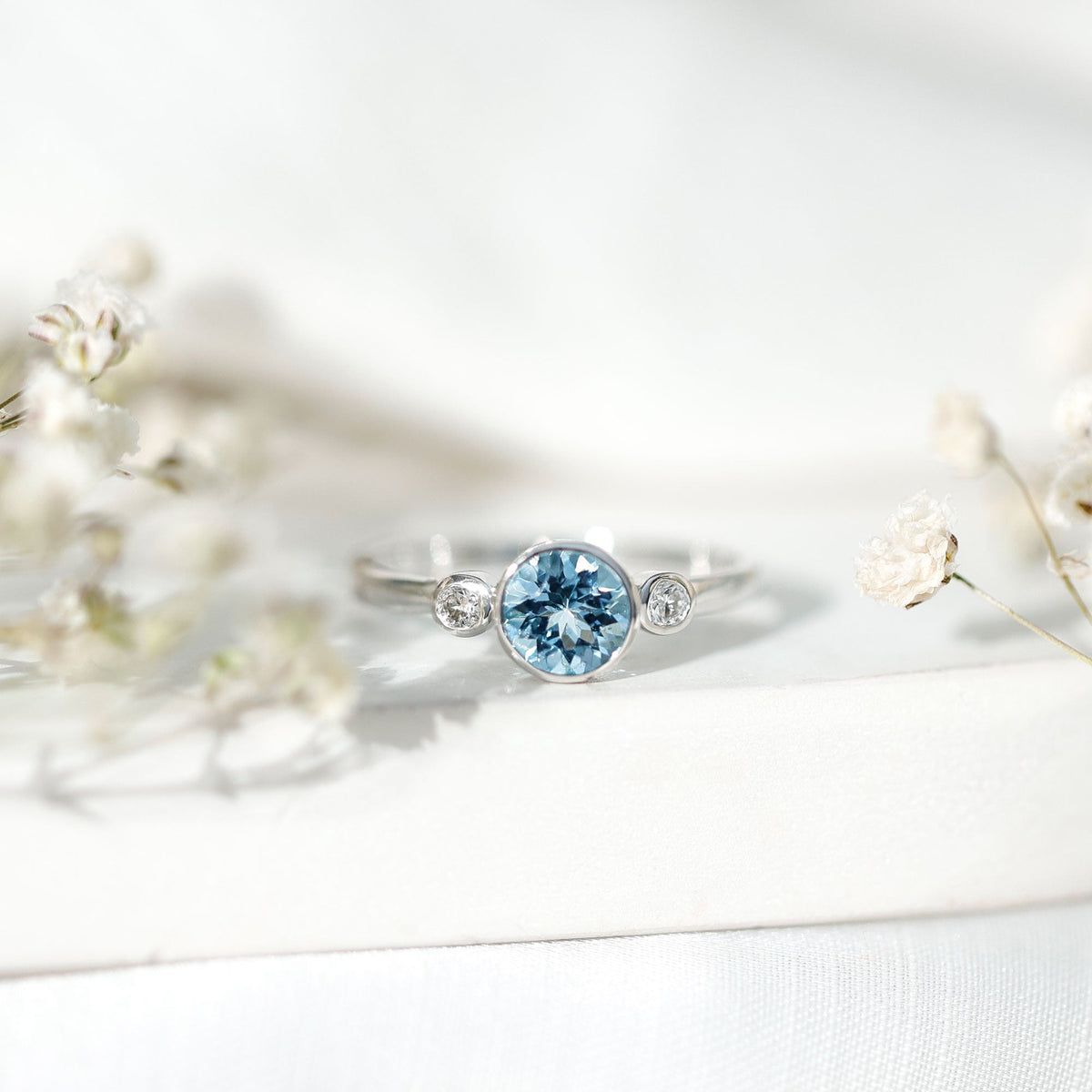 Bezel set real aquamarine and diamond engagement ring by Rosec Jewels, featuring a blue aquamarine gemstone and sparkling diamonds.