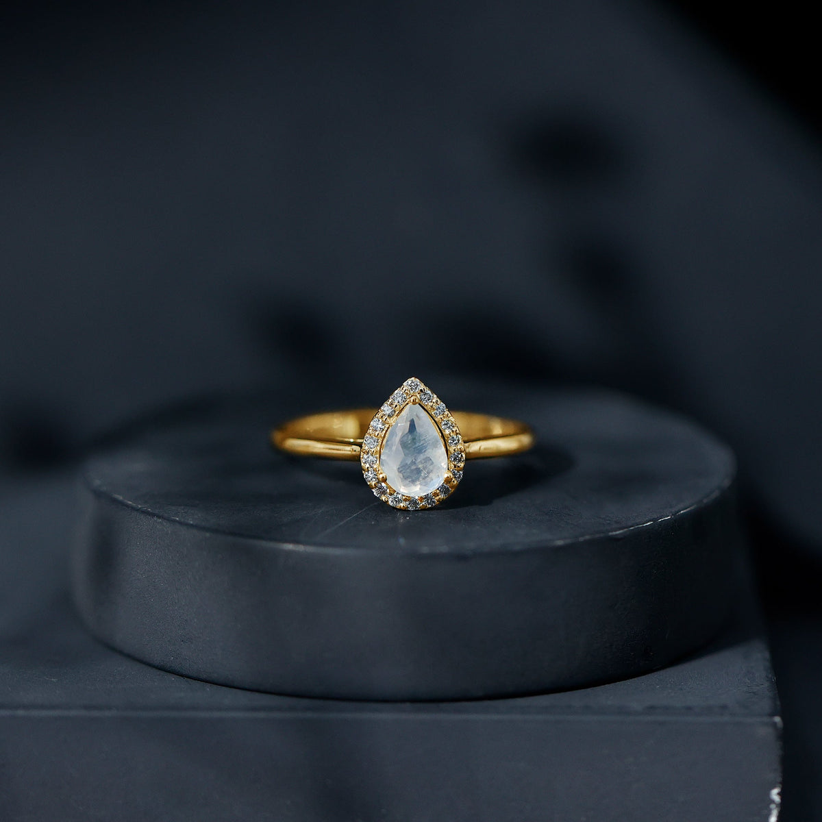 Pear-shaped moonstone halo engagement ring with diamond accents from Rosec Jewels, featuring intricate metalwork and a polished finish.