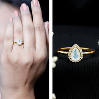 Pear-shaped moonstone halo engagement ring with diamond accents, featuring Rosec Jewels branding and intricate band details.