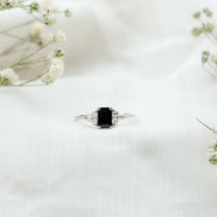 Emerald cut black diamond solitaire ring with diamond trio accents by Rosec Jewels, showcasing a sleek black gemstone setting.