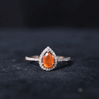 Real 0.6 carat fire opal teardrop engagement ring with diamond halo in yellow gold, featuring a sparkling gemstone and intricate design.