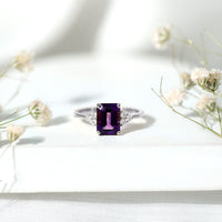 Emerald cut 1.4 carat amethyst engagement ring with diamond trio setting from Rosec Jewels, showcasing a silver band and vibrant purple gemstone.
