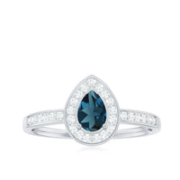 Pear-shaped London Blue Topaz engagement ring with diamond halo by Rosec Jewels, featuring a silver band and intricate detailing.