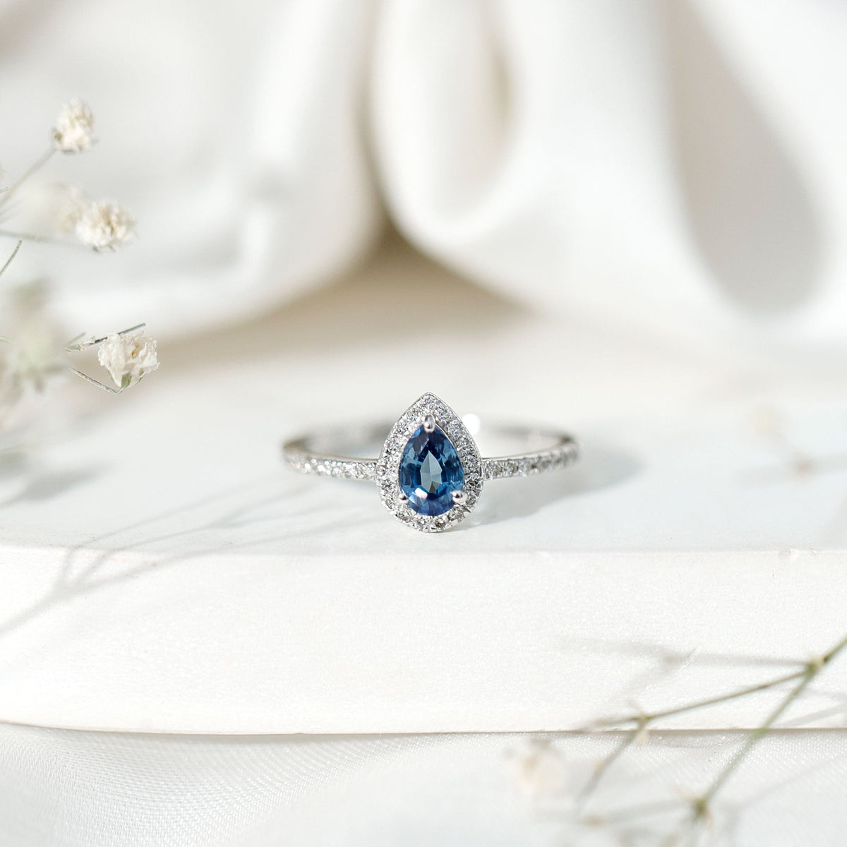 Natural half carat blue sapphire teardrop engagement ring with diamond halo, featuring a rose gold band and intricate detailing.