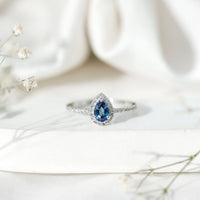 Natural half carat blue sapphire teardrop engagement ring with diamond halo, featuring a rose gold band and intricate detailing.