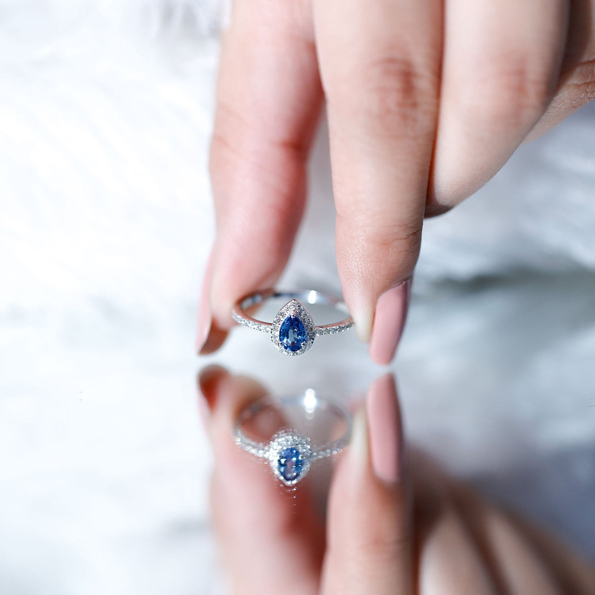 Natural half carat blue sapphire teardrop engagement ring with diamond halo, featuring intricate silver band and sparkling accents.