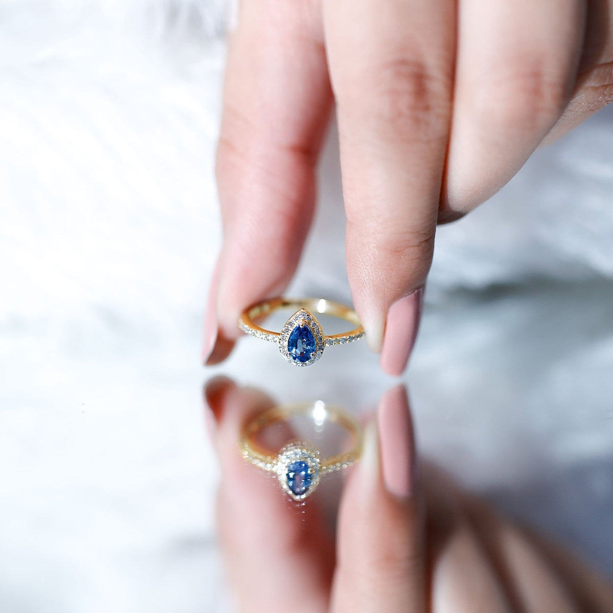 Natural half carat blue sapphire teardrop engagement ring with diamond halo, featuring a silver band and intricate detailing.