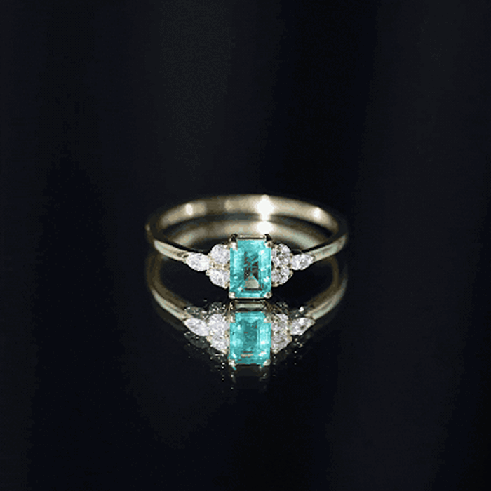 Emerald cut emerald engagement ring with diamond trio, featuring a white gold band and intricate detailing from Rosec Jewels.