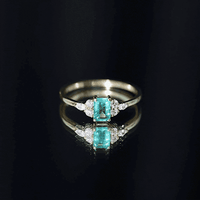 Emerald cut emerald engagement ring with diamond trio, featuring a white gold band and intricate detailing from Rosec Jewels.