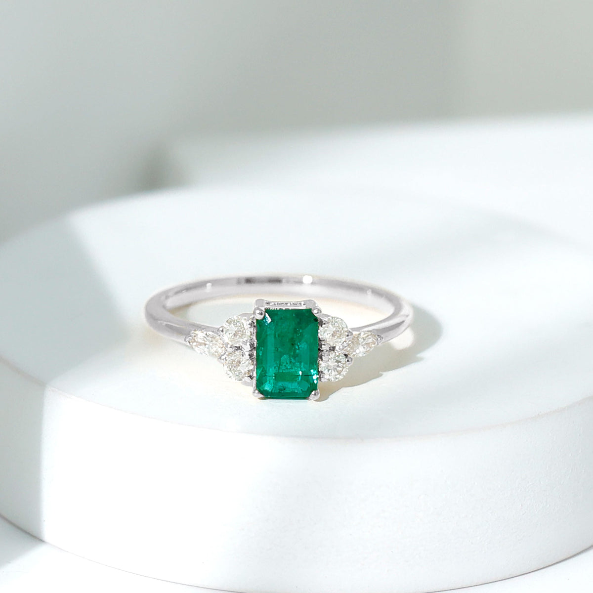 Emerald cut emerald engagement ring with a diamond trio accent, featuring a sleek band and rose gold finish from Rosec Jewels.